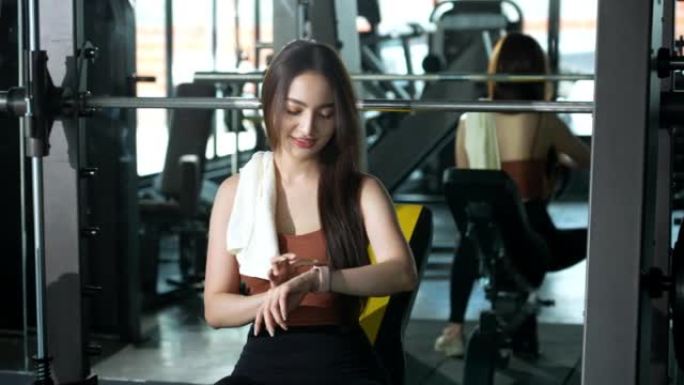 一名亚洲妇女在健身房休息，在健身时间用减肥机锻炼后用毛巾擦干脸