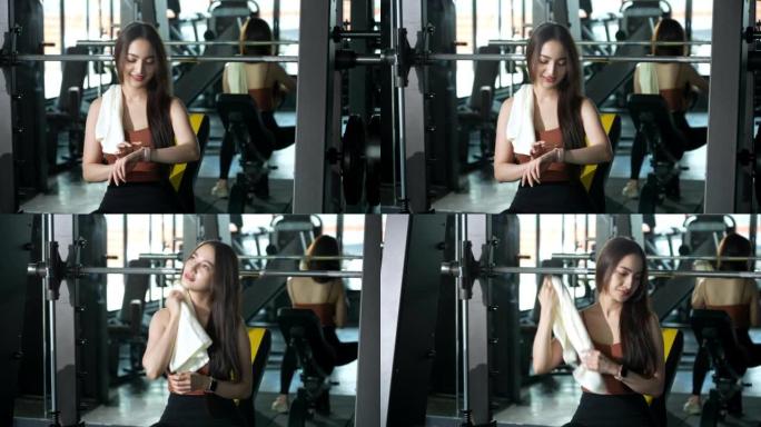 一名亚洲妇女在健身房休息，在健身时间用减肥机锻炼后用毛巾擦干脸