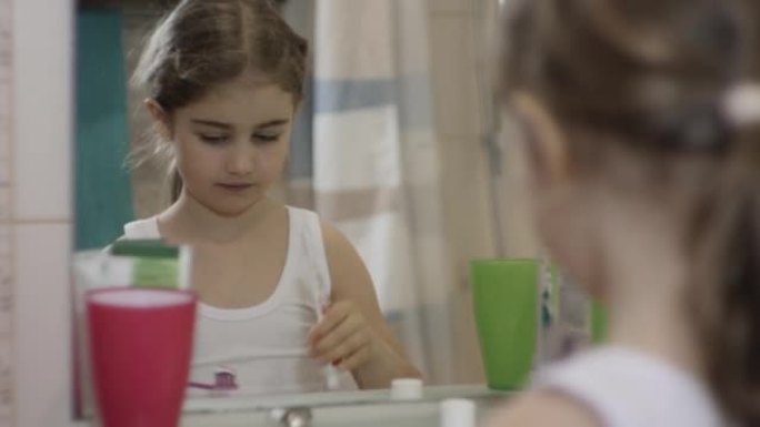 孩子在浴室刷牙。特写肖像年轻的小女孩在浴室刷牙看着镜子反射。日常口腔卫生。快乐肖像可爱高加索无牙