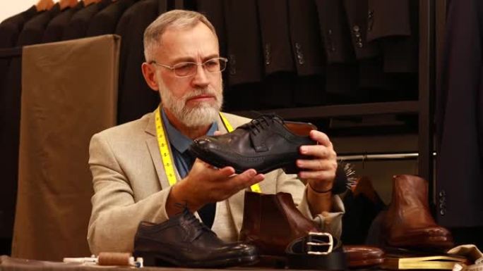 灰胡子的老好看的男人在工作室穿漂亮的西装，检查手工制作的意大利鞋的质量