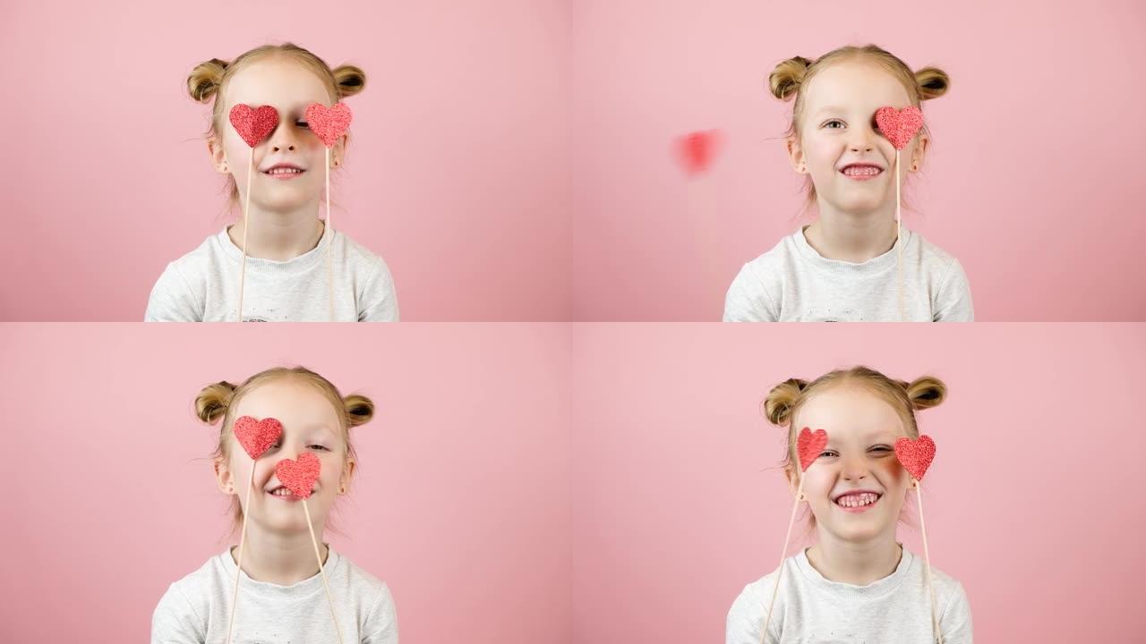 有趣的金发小女孩微笑着玩粉色背景的红心玩具。情人节或母亲节概念