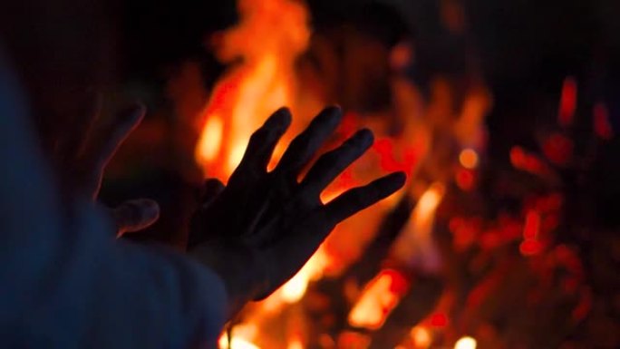 篝火近距离拍摄女人的手。在夏夜背景下，波光粼粼的篝火与游客坐在海滩明亮的篝火旁。旅游活动和周末概念