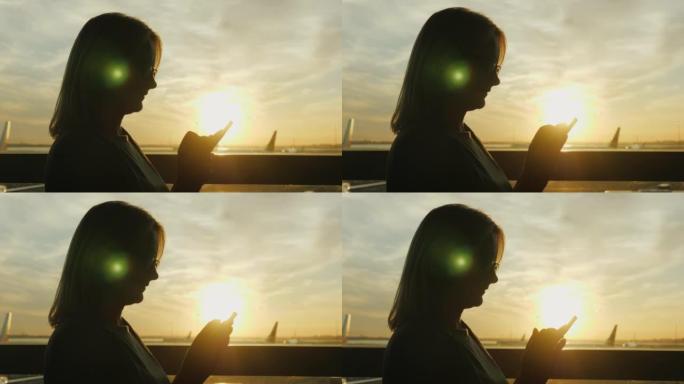 机场航站楼一个大窗户上的一名妇女的剪影。使用智能手机