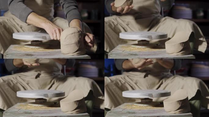 一个无法辨认的男性陶工用线切割柔软的粘土块，并从其中形成球，以便在陶工的轮子上建模。制作特写的陶器。
