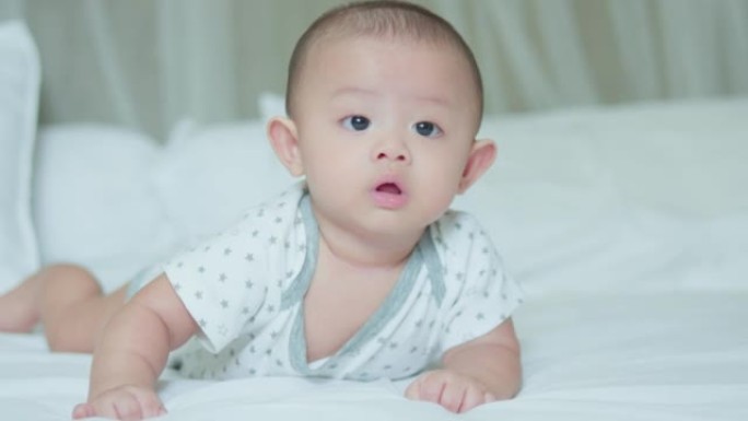 幸福的家庭，可爱的亚洲新生婴儿躺在白色床上爬行玩耍。天真的小新婴儿可爱。父母身份和母亲节概念。