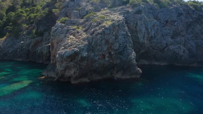 无人驾驶飞机在伊维萨岛的岩石悬崖海岸线和蓝色海洋周围飞弧