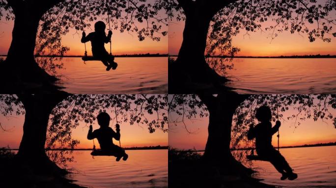 剪影小男孩玩秋千，悬挂在日落背景的树上。