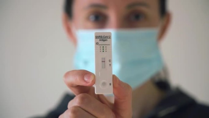 医用口罩中的女性显示带有试剂的快速抗原测试盒，用于检测冠状病毒感染，结果为阴性