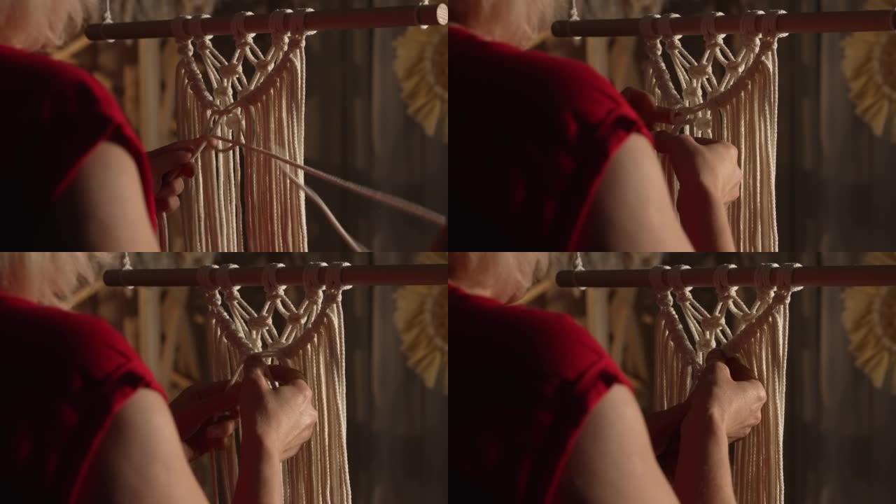 女人在自己的家庭车间的棍子上编织图案的花边。女性双手打结，形成一条线。手工制作的概念。妇女在针线活过