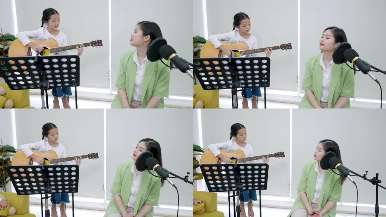 坐在高脚椅上的小年轻亚洲女孩正在弹吉他，而美丽的年轻亚洲老师正坐在麦克风前唱歌。