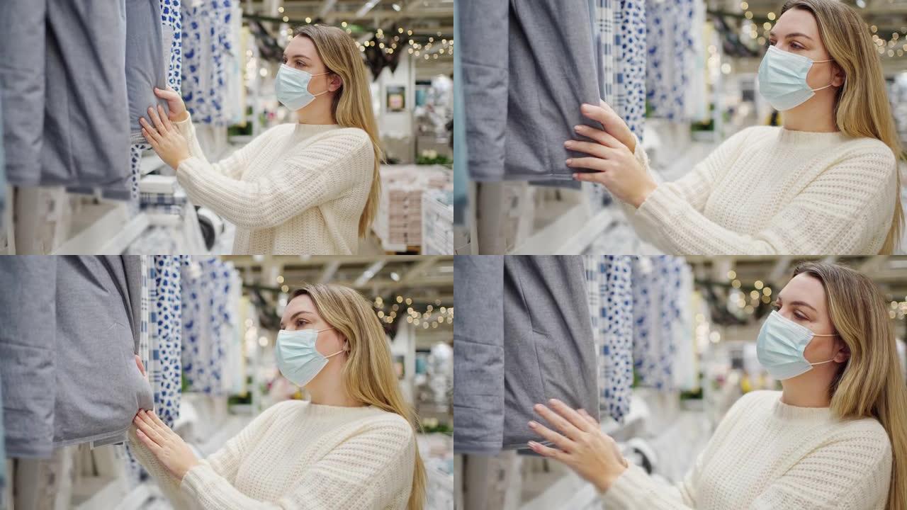 年轻女子戴着防护口罩在商店里特写选择家用纺织品、床上用品