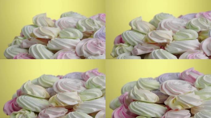 黄色背景上旋转的甜蛋白酥皮漩涡。糖果中的甜蛋白酥皮黄色，粉红色和紫色。蛋白质和糖饼干的特写镜头。慢动
