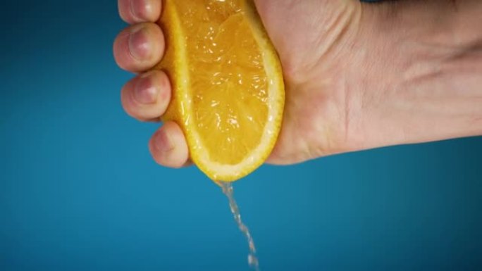 一个男人的手在蓝色背景上从半个橙色中榨汁的特写镜头