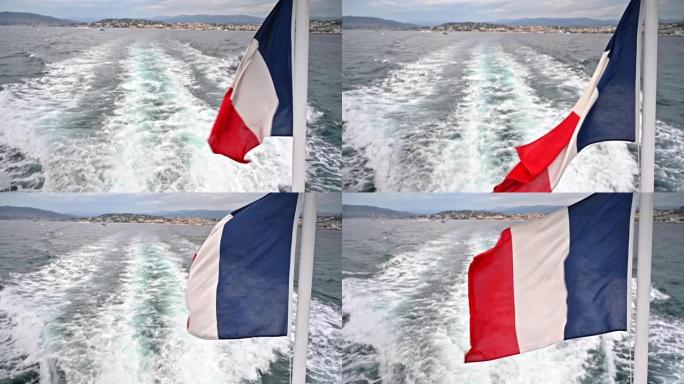 漂浮的船上随风飘扬的法国国旗。远处的戛纳。法国。慢动作