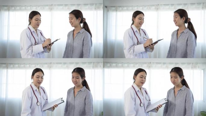 4K 50fps，白人亚裔女医生站在医院检查室对一名身穿长袖衬衫的长发亚裔患者做笔记 ....
