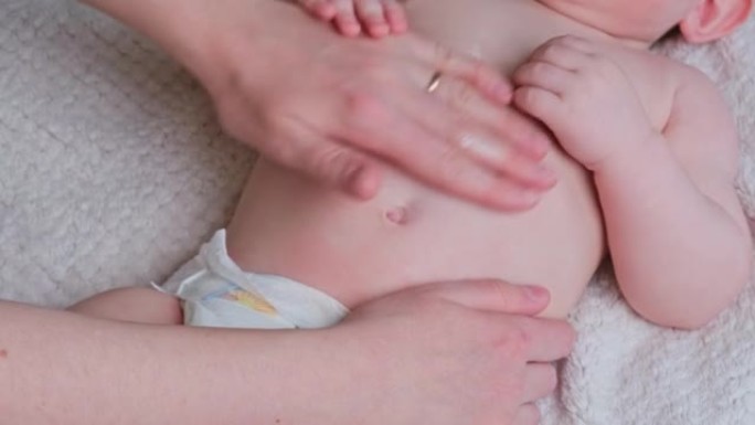 母亲的手在婴儿身上涂抹奶油。妈妈在沙发上按摩一个八个月大的小孩