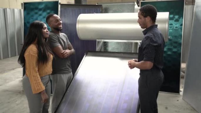 混合种族推销员在工厂陈列室向美国黑人夫妇展示了大型热太阳能热水设备