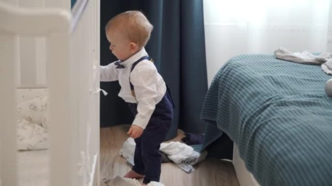 蹒跚学步的孩子用衣服探索衣柜的抽屉，一岁的男婴将衣服从壁橱中拉出并扔到地板上。
