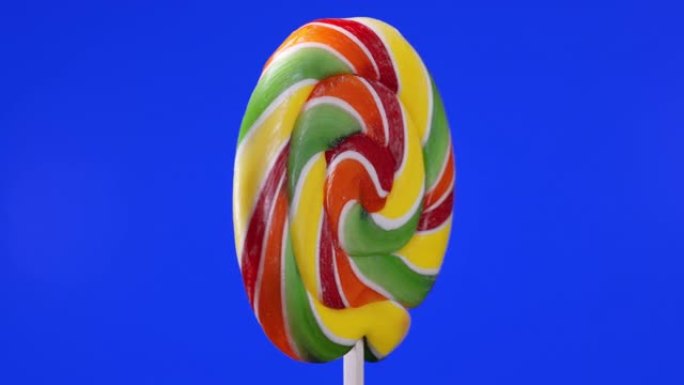 蓝色背景上螺旋水果棒棒糖的旋转。焦糖棒棒糖。儿童糖果。宏观。童年概念。