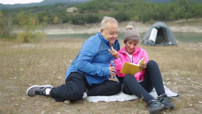 快乐的老年夫妇在树林里露营时看书 -- 老年人旅行生活方式