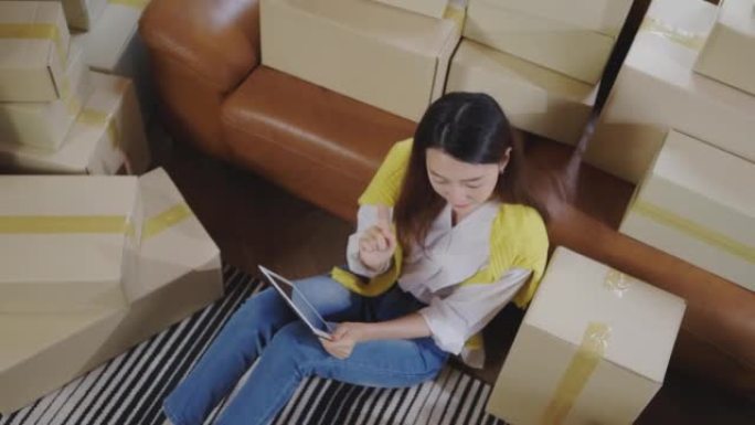 一名年轻的亚洲女性用数码平板电脑与消费者沟通，在自家客厅里在线销售产品。