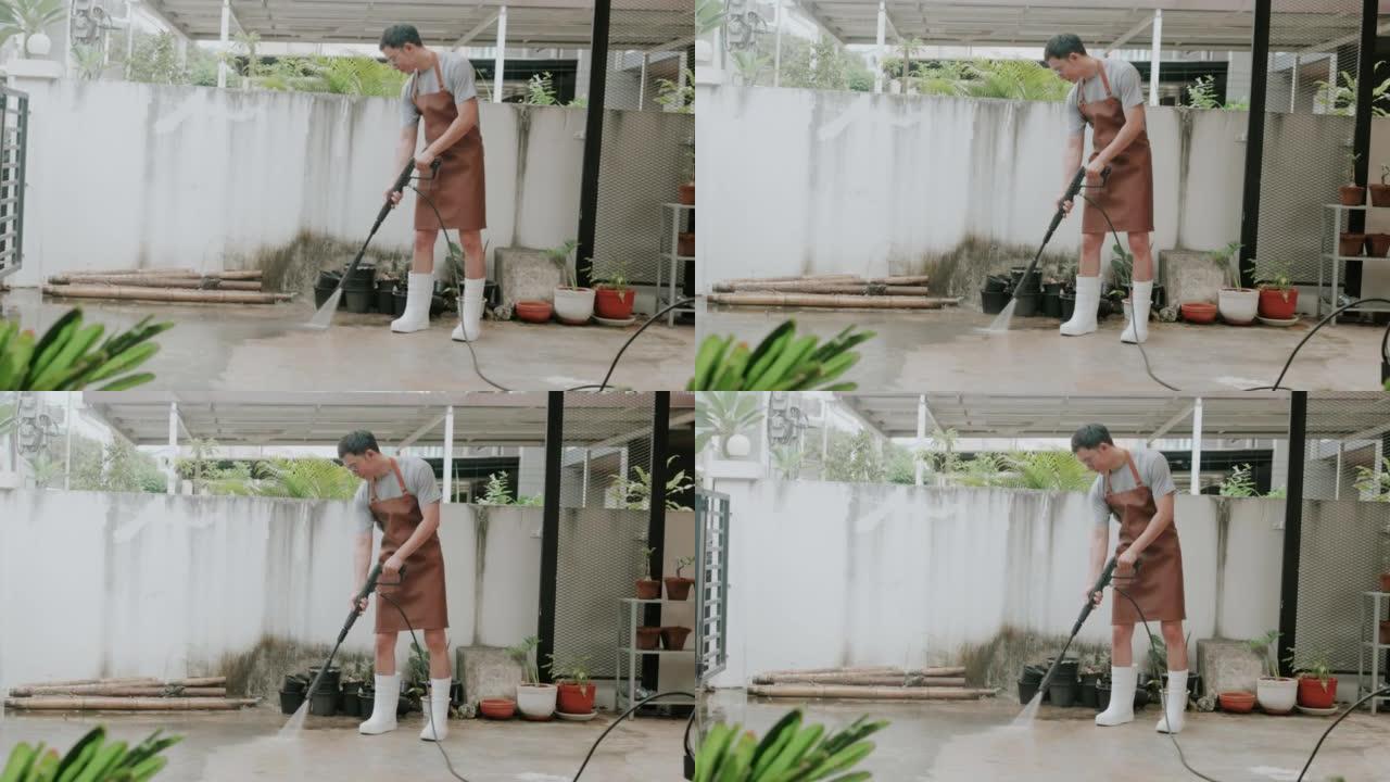 亚洲男子用高压动力清洗机清洁车库地板。