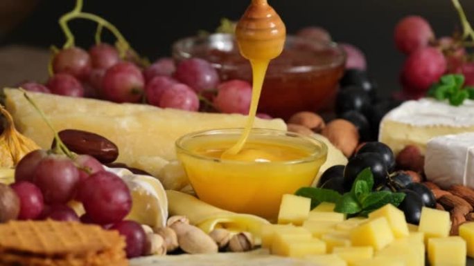 奶酪盘和蜂蜜。将木棍浸入装有液体蜂蜜的玻璃碗中，从木勺中倒入。用各种类型的硬奶酪制备奶酪拼盘-卡门培