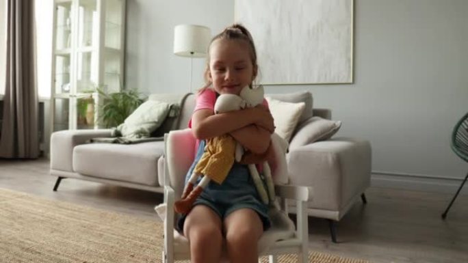 兴奋的孩子坐在摇椅上，坐在家里的客厅里玩她的毛绒玩具
