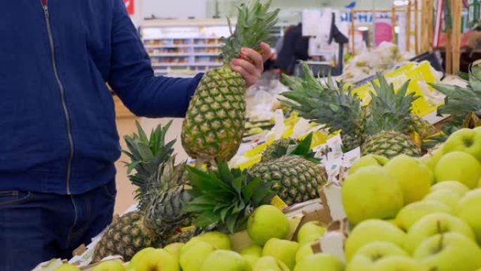 水果摊市场上的顾客选择菠萝。晚餐买水果。水果摊商店里的一个人选择新鲜的菠萝做饭