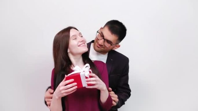 庆祝情人节的幸福夫妇。戴眼镜的微笑男人拥抱美丽的女人，并赠送红色礼品盒。