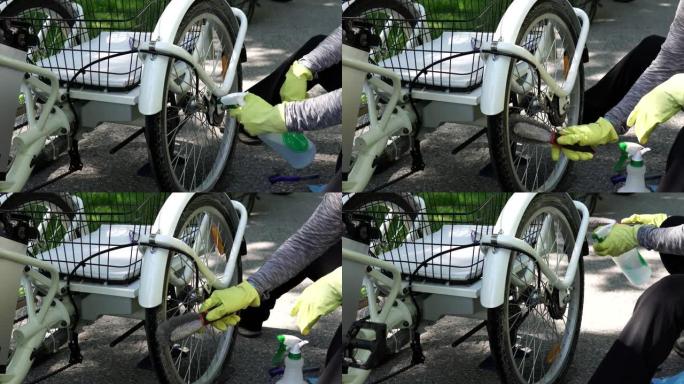 戴着黄色手套的骑自行车的人在夏天在外面清洁电动自行车后轮。骑手照顾电动自行车车轮。动力电池和控制器齿