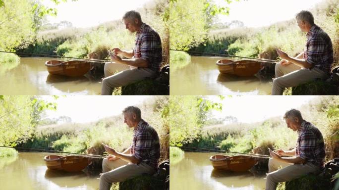 成熟的男人在阳光明媚的夏日河钓鱼和使用智能手机