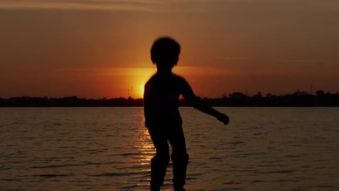 SLO MO小男孩在日落时在海滩上跳舞。