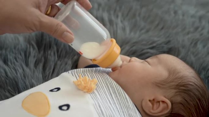 4k，一个刚出生的2个月大的亚洲人正在母亲喂养的瓶子里哺乳，睡在灰色的地毯上。