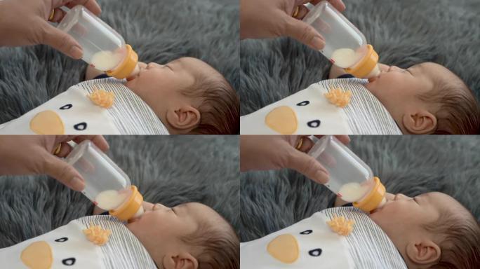 4k，一个刚出生的2个月大的亚洲人正在母亲喂养的瓶子里哺乳，睡在灰色的地毯上。