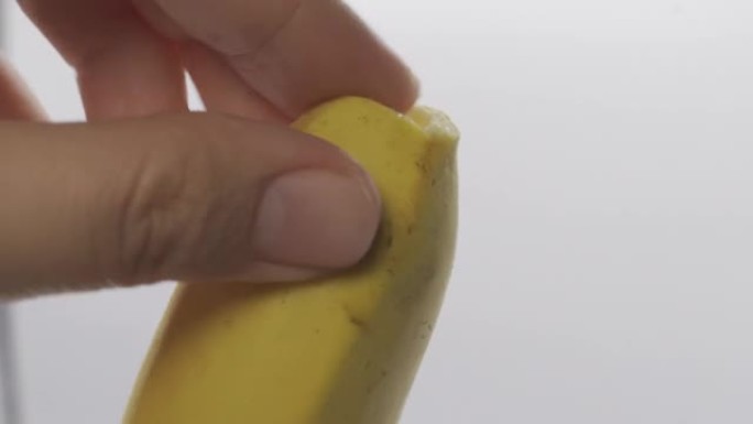 女人的手剥香蕉吃。成熟和黄色的新鲜香蕉。带有工作室感觉的白色背景。宏观拍摄。