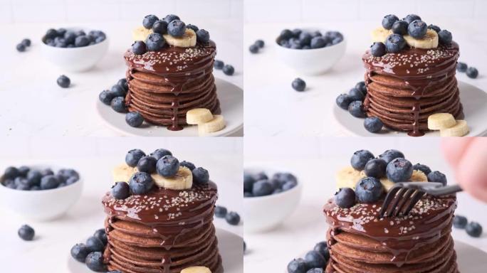 巧克力煎饼，巧克力酱，蓝莓和香蕉堆叠在白色盘子上。