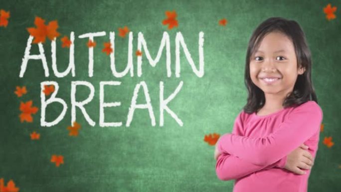 漂亮的小女孩在教室里微笑着，在黑板和秋叶上露出拇指，上面写着秋假的文字