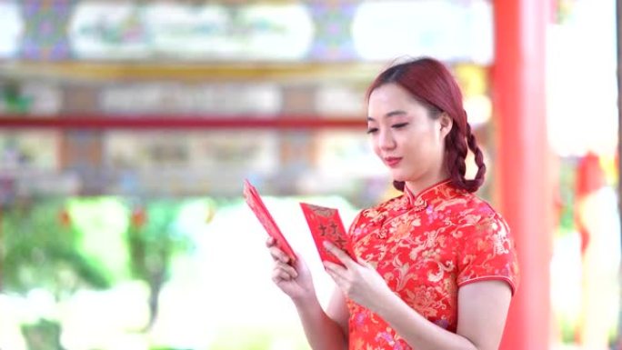 亚洲年轻女子，穿着红色的中国传统旗袍装饰，拿着红色的旗袍信封，上面写着中文的祝福是一个好运气的中国新