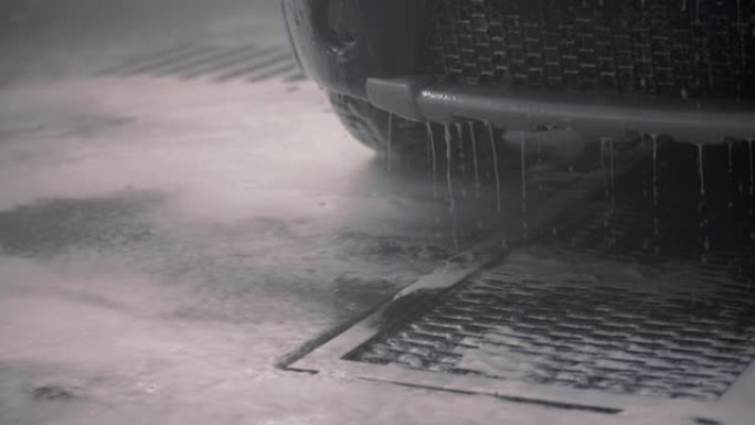 从汽车保险杠上滴下来的带有清洁剂的水。自助室内洗车流程。具有选择性聚焦和慢动作的特写视图。