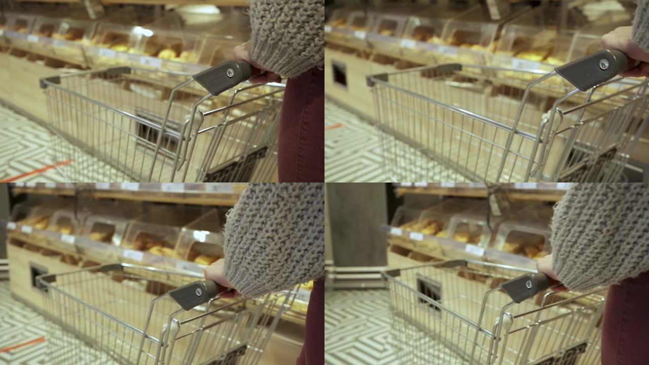 一位年轻女性购物者的手在超市的过道中移动一辆空手推车的特写镜头