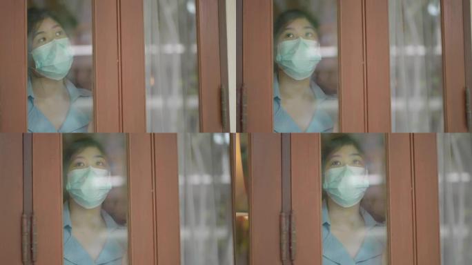 戴口罩的亚洲女孩在屋内用悲伤的眼神看着外面