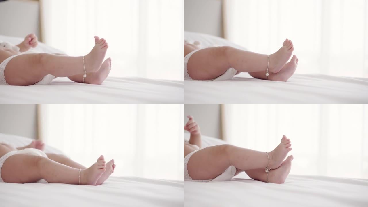 穿着尿布的无辜亚洲新生儿的特写镜头，躺在柔软的床上，抬起穿着可爱的脚链的腿