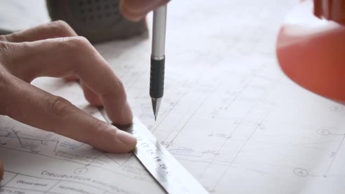 对工作图纸进行调整的过程。工程师的手使用尺子和自动铅笔对设计文档进行更改。标尺铅笔卷尺和安全帽。
