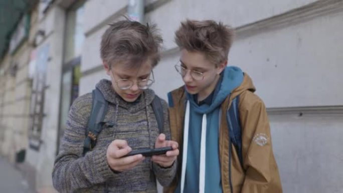 十几岁的男孩站在公共汽车站并使用智能手机