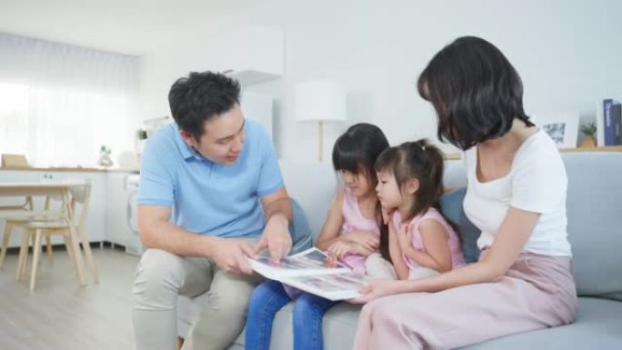 亚洲家庭看旧相册上的照片回忆过去。年轻美丽的夫妇坐在一起，带着小女儿翻动相册的页面，享受记忆的关系记