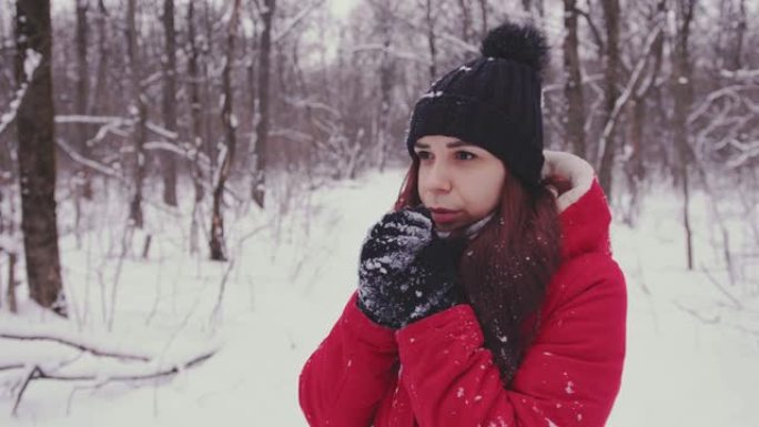 年轻的冷冻女人穿着头球和红色夹克。成年女性在寒冷的天气里用手套加热双手