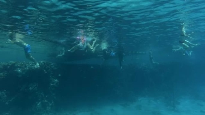 一群游客在阳光下的珊瑚礁旁边的酒店码头玩得开心。度假者在珊瑚旁边的海里游泳。水下射击