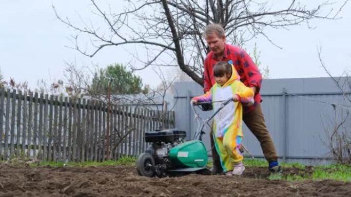 穿着独角兽服装的孩子帮助年迈的祖父在花园里工作，用耕种者耕种土地