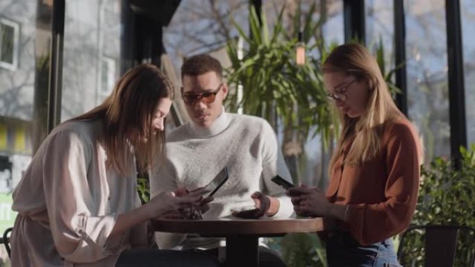 咖啡馆酒吧里的三个朋友用电话。看着智能手机对周围环境的无意识 ..